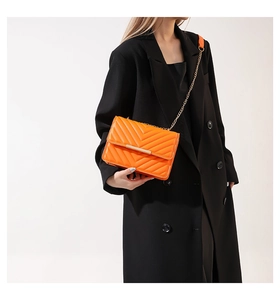 Detail of vibrant orange quilted crossbody bag with gold chain on model in black suit