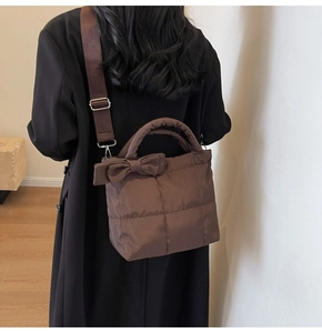 Close-up of brown quilted tote bag with a bow decoration and wide strap on model
