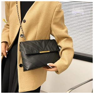 Close-up of black quilted shoulder bag with gold hardware on a beige blazer