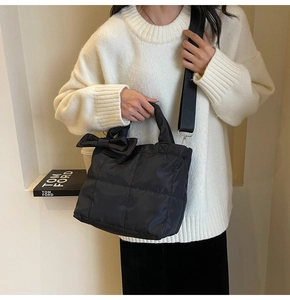 Detail of a black quilted tote bag with a soft bow and a wide adjustable shoulder strap