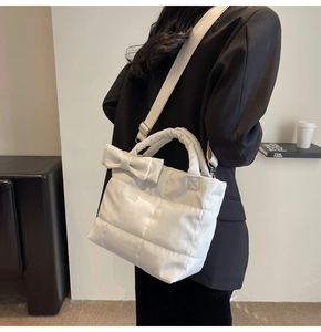 Detail of white quilted puffer tote with side bow decoration and soft puffed texture