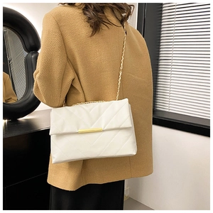 Close-up of white quilted leather crossbody bag with gold chain strap on a camel coat