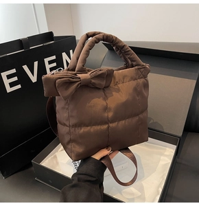 Detail of a brown quilted tote bag with a decorative side bow and padded handles