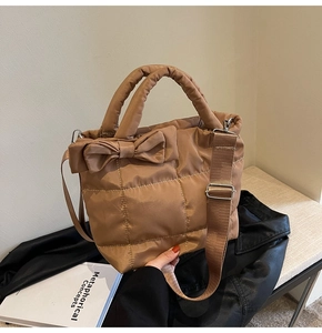 Detail of brown quilted puffer tote bag featuring a decorative bow and thick top handles
