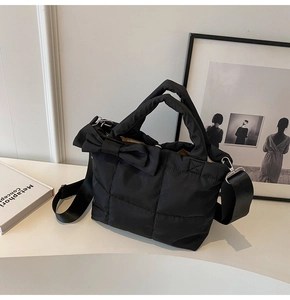 Close-up of black quilted puffer tote bag with decorative side bow and wide strap
