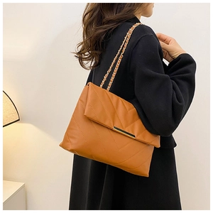 Caramel quilted shoulder bag with gold chain strap shown on a model in a warm interior