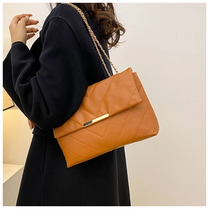 Detail of caramel brown quilted leather shoulder bag with golden chain strap on a model