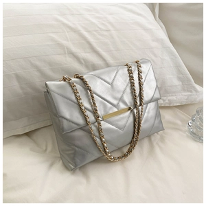 Detail of silver quilted shoulder bag with V-pattern and golden chain strap on soft bedding