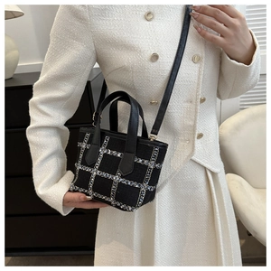 Detail of black tweed crossbody bag with gold pattern on a white texture blazer