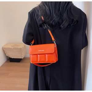 Detail of an orange textured flap bag with square embossing on a black blazer