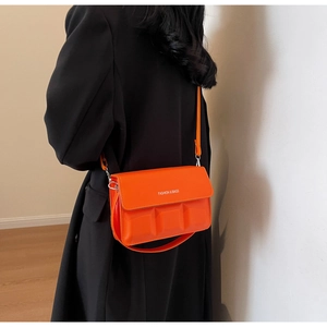 Detail of bright orange square crossbody bag with embossed texture on black coat