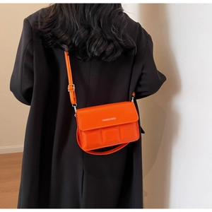 Detail view of bright orange square crossbody bag with embossed texture on black coat