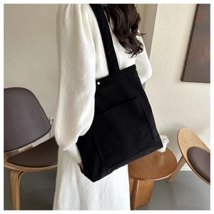 Detail of black corduroy tote bag showing soft ribbed texture and large front pocket