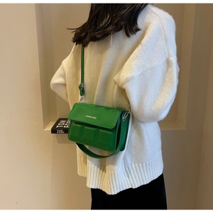 Detailed view of green crossbody bag with chocolate relief texture on white sweater