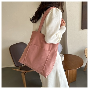 Detailed close-up of a pink corduroy tote bag with large pocket in a cozy cafe setting