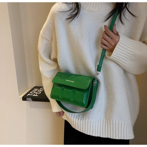 Close-up of green embossed leather square bag with fashion text on a white knit sweater
