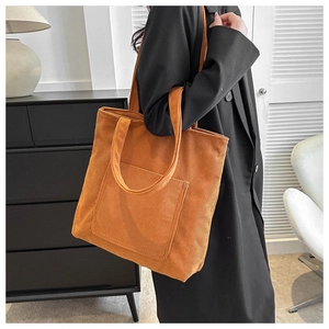 Detail of orange corduroy tote bag showing ribbed texture and front pocket on shoulder