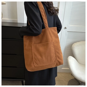 Detailed texture of brown corduroy tote bag showing front pocket and wide shoulder strap