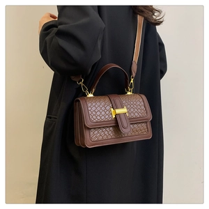 Detail of brown woven shoulder bag featuring a gold metal buckle and adjustable strap