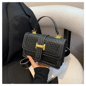Close-up of black crossbody bag with golden H buckle and stylish woven strap detail
