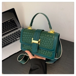 Detail of dark green woven texture handbag with gold metal lock and wide canvas strap