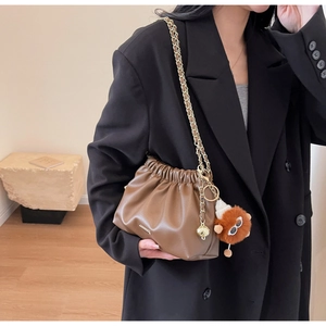 Detail of soft brown PU leather bag with gold chain and plush lion charm on black blazer