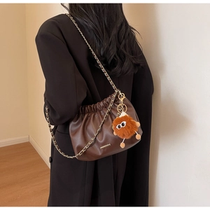 Detail of soft leather brown bucket bag featuring a gold chain strap and cute monster charm