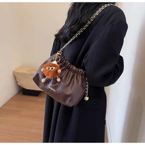 Detail of dark brown drawstring bag with plush monster charm and chain strap