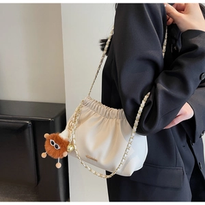 Detail of cream bucket bag with lychee texture, gold chain and plush monster charm