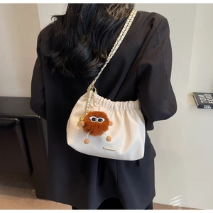 Detail of white drawstring bucket bag with gold chain and plush monster charm