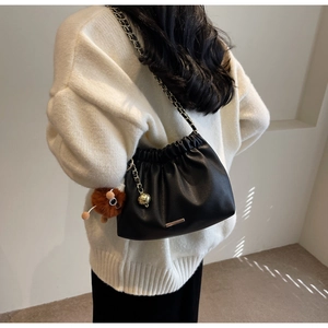 Detail of black leather dumpling bag with metal chain strap and cute bear charm pendant