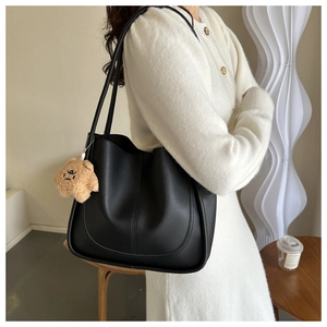 Detail of black tote bag with vertical stitching and a cute khaki teddy bear charm