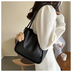 Close-up of black PU leather tote bag with U-shaped stitching and plush bear charm