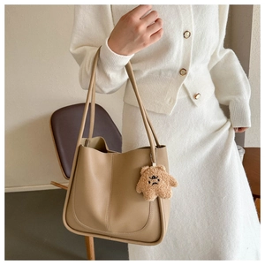 Detail of khaki tote bag featuring smooth PU leather texture and a cute bear pendant