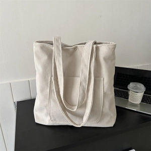 Minimalist off-white corduroy tote bag with front pocket on a desk, casual daily style