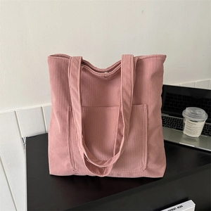 Pink corduroy tote bag with large front pocket and laptop on a minimalist desk setup