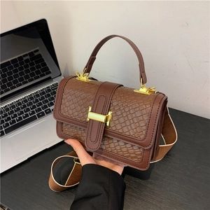 Brown woven crossbody bag with gold buckle and wide strap on an office desk