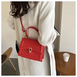 Detail of red leather crossbody bag with golden ring clasp against a white coat