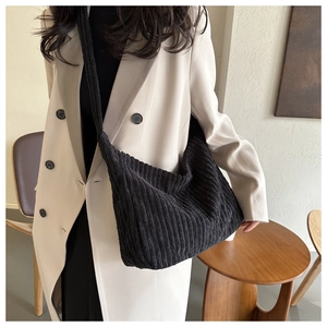 Détail du sac bandoulière en velours côtelé noir à texture verticale sur un trench-coat beige