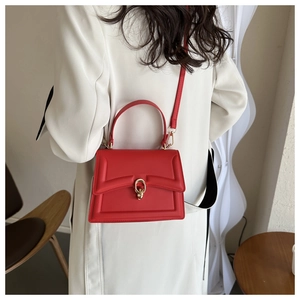 Red leather handbag with gold metal clasp shown on a shoulder in a stylish modern room