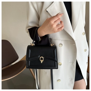 Detail of a black leather crossbody bag with gold ring buckle worn over a white coat