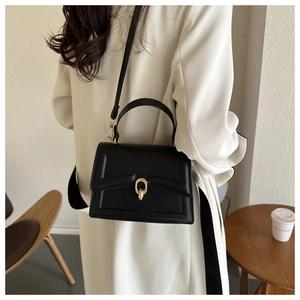 Detail of a black leather crossbody bag with a gold twist-lock on a beige trench coat