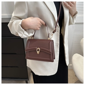 Detail of dark brown crossbody bag with gold hardware worn by model in white blazer