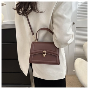 Detail of dark brown quilted leather handbag with gold metal clasp on white blazer