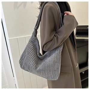 Gros plan sur un sac hobo en velours côtelé gris à larges rayures porté avec un blazer