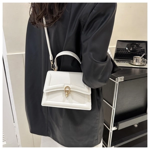 Close-up of white leather handbag with gold ring buckle worn as a crossbody bag