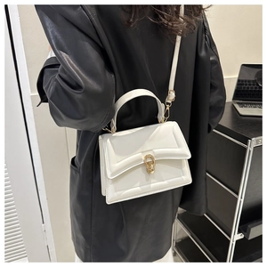 White leather crossbody bag with gold metal lock shown as a shoulder style on model