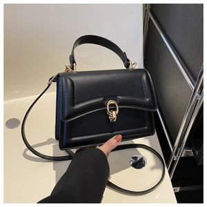 Detail of a black structured handbag with matte finish and gold oval clasp closure