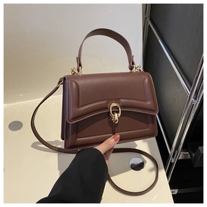 Close-up of deep brown leather handbag featuring a geometric flap and gold metal ring buckle