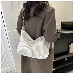 Détail du sac cabas en velours côtelé blanc porté sur un manteau marron dans un bureau